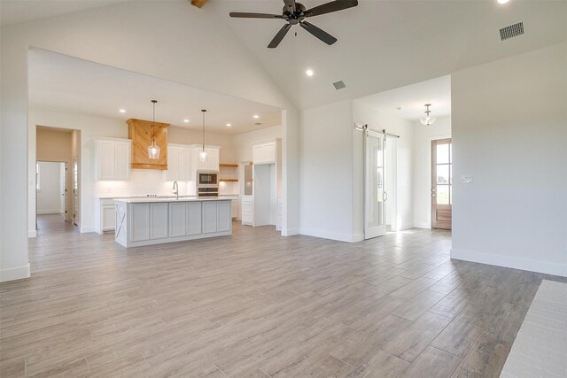 kitchen featuring white cabinetry, hanging light fixtures, a kitchen island with sink, stainless steel oven, and built in microwave