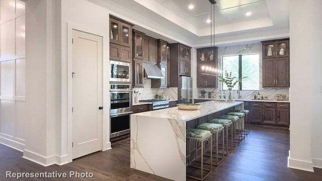 kitchen with a breakfast bar area, decorative light fixtures, appliances with stainless steel finishes, a kitchen island, and backsplash