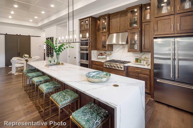 kitchen with appliances with stainless steel finishes, a breakfast bar, decorative light fixtures, light stone countertops, and a barn door