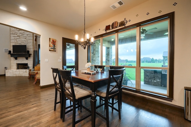 dining space featuring dark wood-type flooring, a notable chandelier, a wealth of natural light, and a stone fireplace