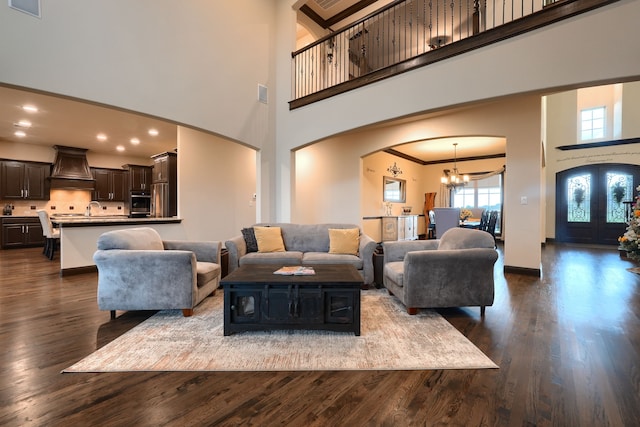 living room featuring a high ceiling, dark wood-type flooring, sink, ornamental molding, and a chandelier