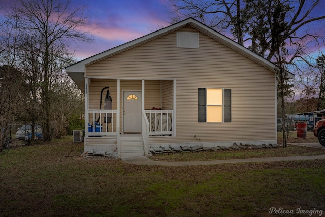 bungalow featuring a yard, a porch, and central air condition unit