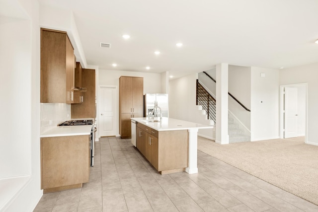 kitchen featuring light carpet, an island with sink, light countertops, stainless steel appliances, and a sink