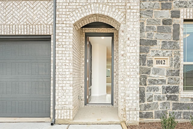 doorway to property with a garage, stone siding, and brick siding