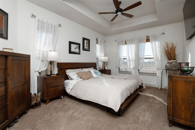 bedroom with light carpet, ceiling fan, and a raised ceiling