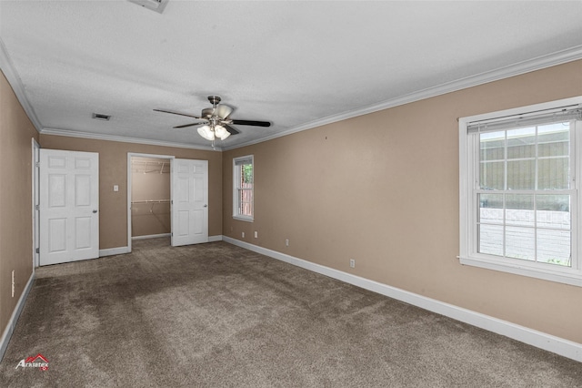 unfurnished bedroom with crown molding, ceiling fan, carpet, a spacious closet, and a closet