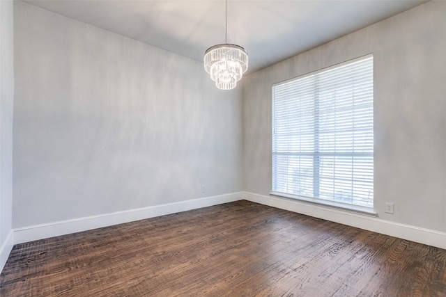 empty room with dark wood-type flooring and a chandelier