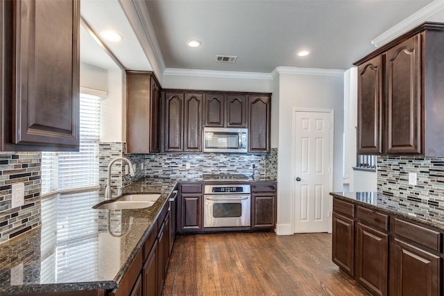 kitchen with dark wood-type flooring, sink, crown molding, dark stone countertops, and appliances with stainless steel finishes