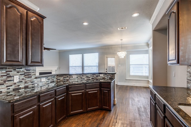 kitchen featuring crown molding, backsplash, dark brown cabinetry, and decorative light fixtures