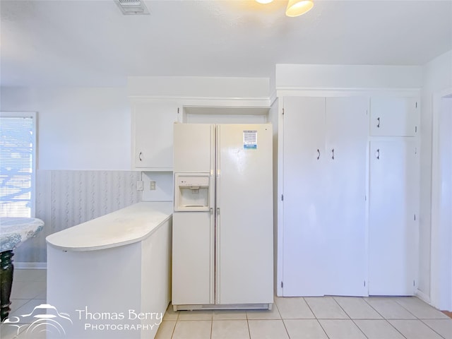 kitchen featuring light tile patterned flooring, white refrigerator with ice dispenser, and white cabinets