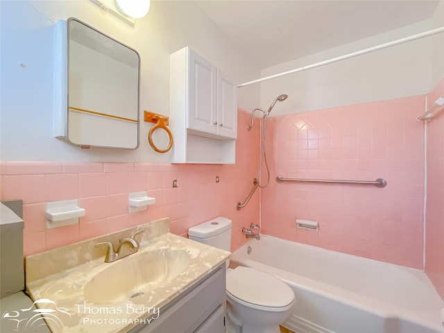 full bathroom featuring tiled shower / bath combo, vanity, tile walls, and toilet