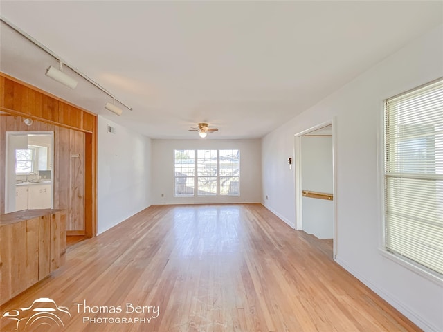 empty room featuring sink, ceiling fan, track lighting, light hardwood / wood-style floors, and wood walls