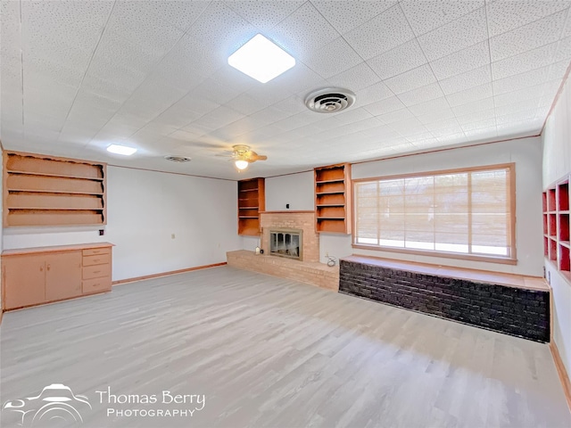 unfurnished living room featuring built in shelves, a fireplace, and light wood-type flooring