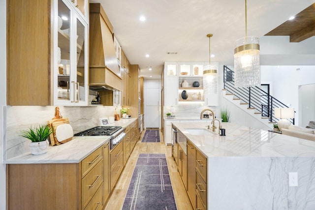 kitchen featuring pendant lighting, stainless steel gas stovetop, sink, light stone counters, and custom range hood