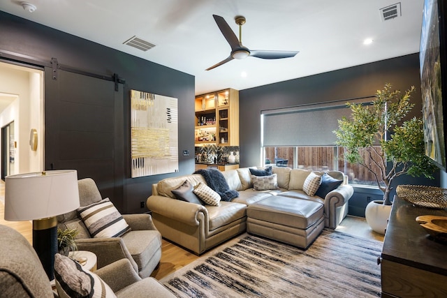 living room with ceiling fan, a barn door, and light hardwood / wood-style floors