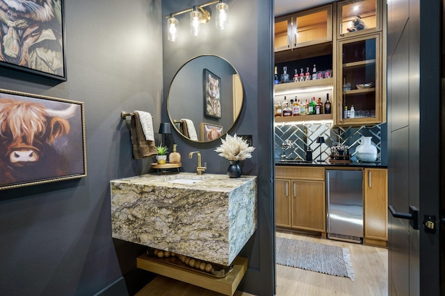 bar featuring sink, stainless steel fridge, decorative backsplash, light stone countertops, and light wood-type flooring