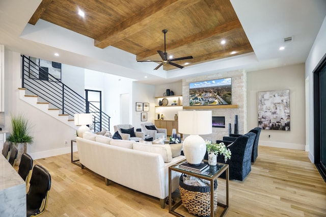 living room featuring wood ceiling, light wood-style floors, stairs, a stone fireplace, and baseboards