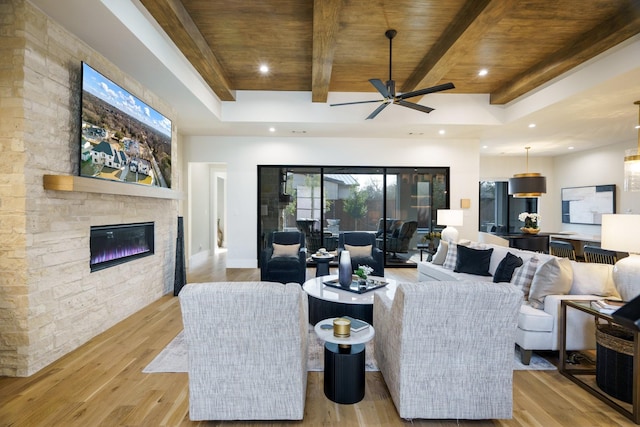 living area featuring wood ceiling, a stone fireplace, ceiling fan, beamed ceiling, and light wood-style floors