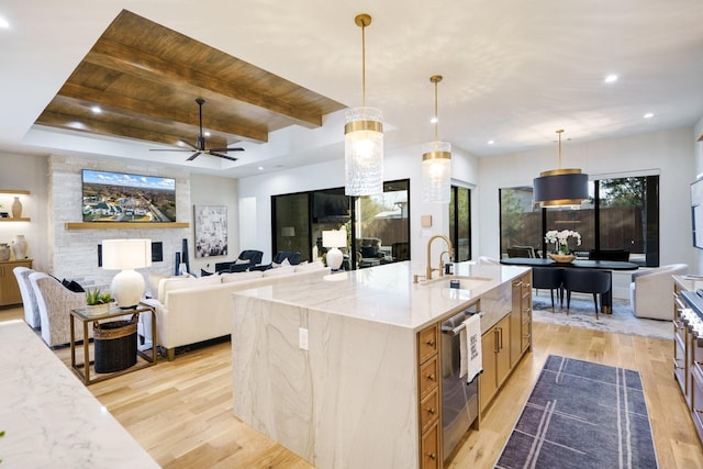 kitchen featuring hanging light fixtures, light stone countertops, sink, and a center island with sink