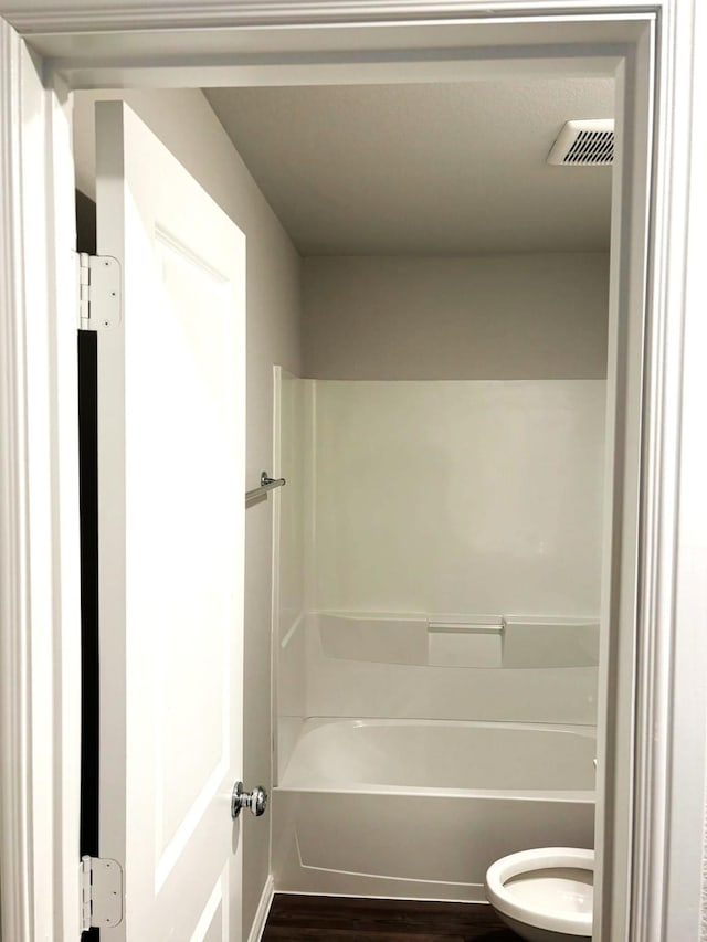 bathroom with toilet, bathing tub / shower combination, and hardwood / wood-style floors