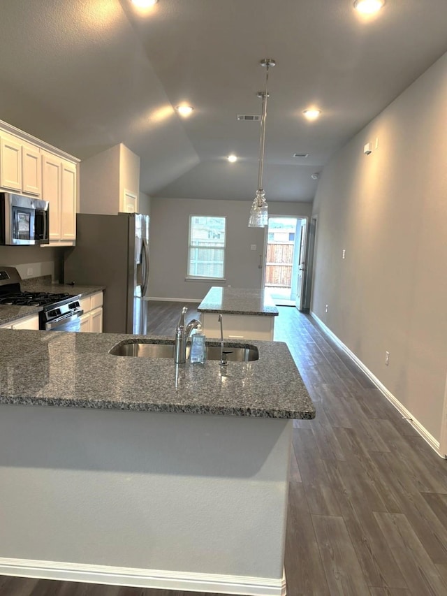 kitchen featuring sink, vaulted ceiling, dark stone counters, stainless steel appliances, and white cabinets