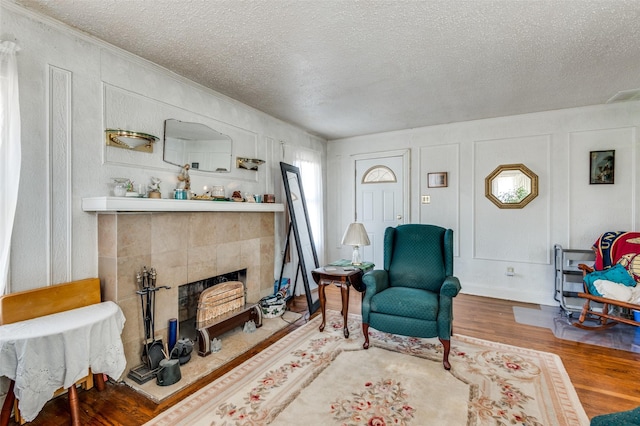 living room with a tiled fireplace, hardwood / wood-style floors, and a textured ceiling