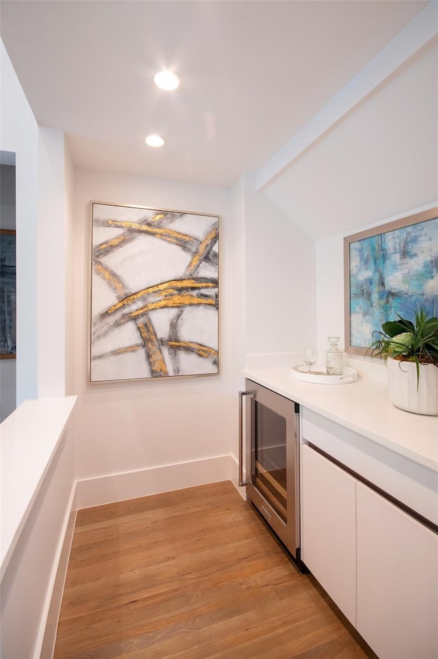 bar with white cabinetry, beverage cooler, and light hardwood / wood-style flooring