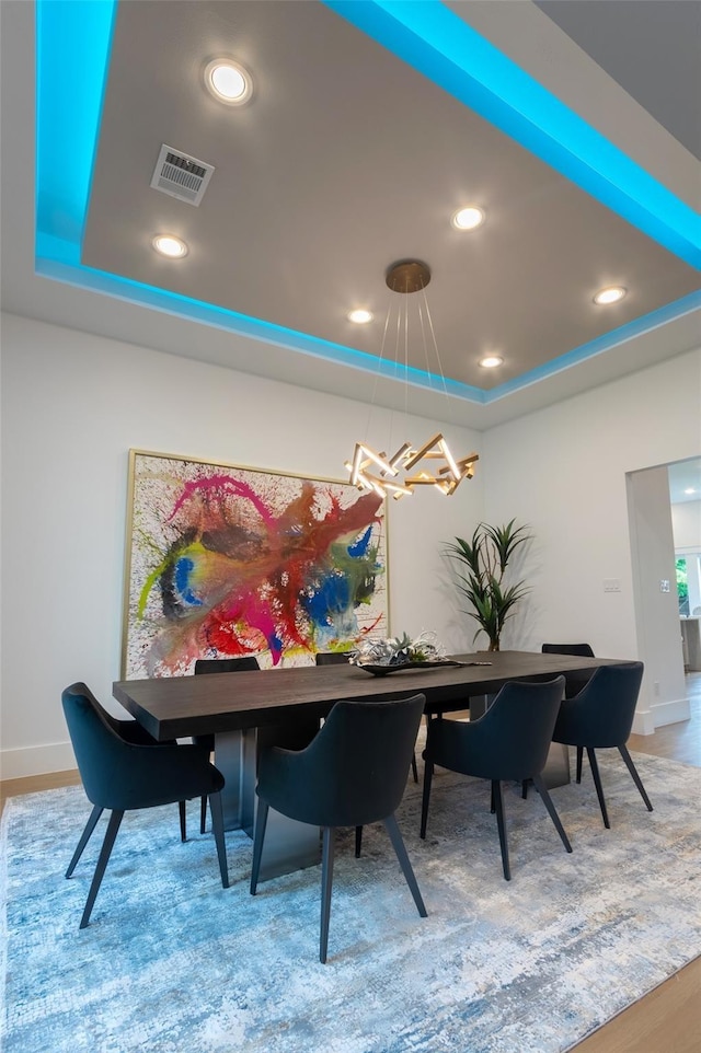 dining space with hardwood / wood-style floors, an inviting chandelier, and a tray ceiling