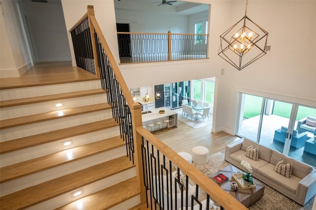 stairway with ceiling fan with notable chandelier, wood-type flooring, and a towering ceiling