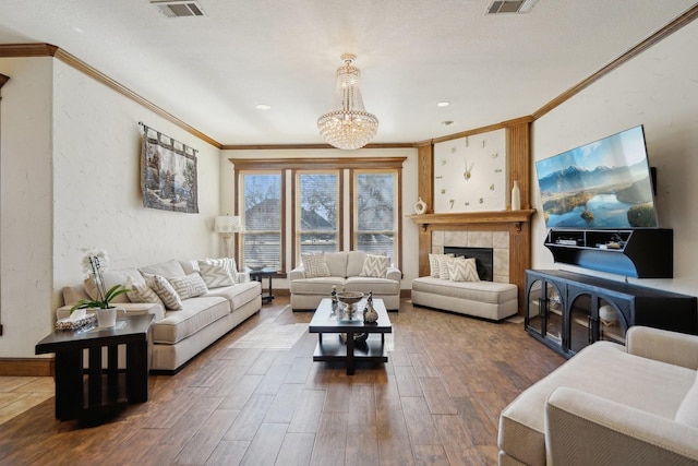 living room with a textured ceiling, a tile fireplace, an inviting chandelier, and crown molding