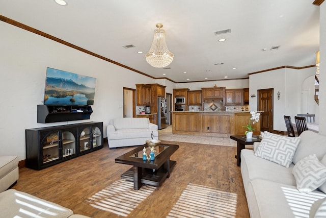 living room with light hardwood / wood-style flooring, ornamental molding, and an inviting chandelier