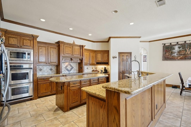 kitchen with light stone countertops, light tile patterned floors, a center island with sink, and tasteful backsplash