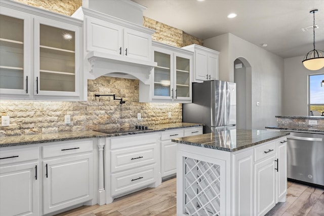 kitchen featuring white cabinets, stainless steel appliances, decorative backsplash, premium range hood, and hanging light fixtures