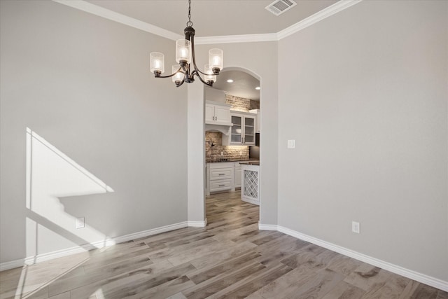 unfurnished dining area with light wood-type flooring, crown molding, and an inviting chandelier