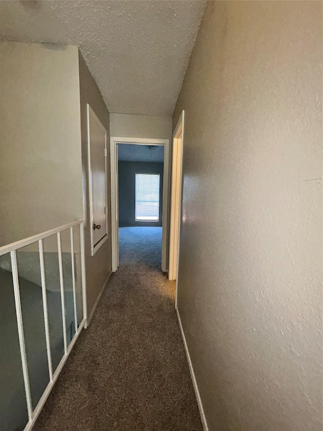 hall with dark carpet and a textured ceiling