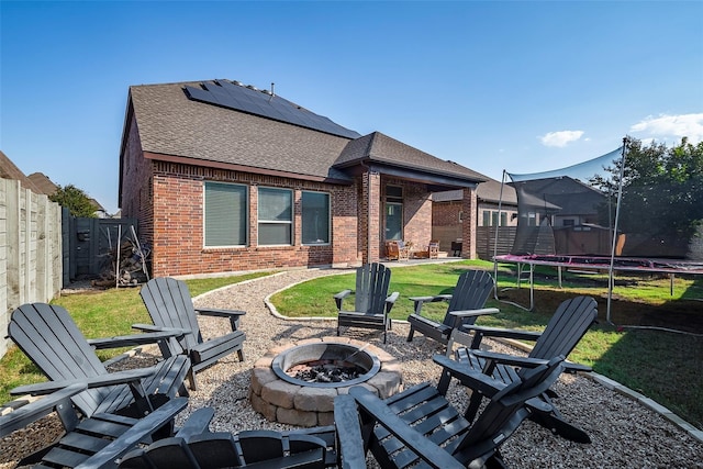 rear view of house with an outdoor fire pit, a patio, a lawn, solar panels, and a trampoline