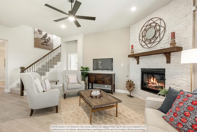 living room featuring ceiling fan, light hardwood / wood-style flooring, and a stone fireplace