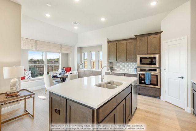 kitchen featuring appliances with stainless steel finishes, sink, light wood-type flooring, tasteful backsplash, and an island with sink