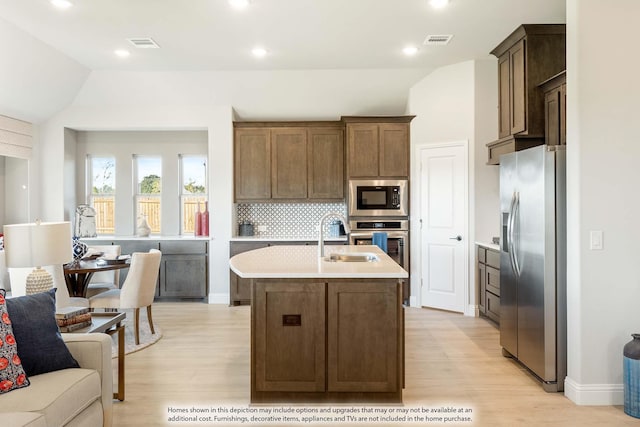 kitchen with appliances with stainless steel finishes, tasteful backsplash, an island with sink, sink, and light hardwood / wood-style flooring