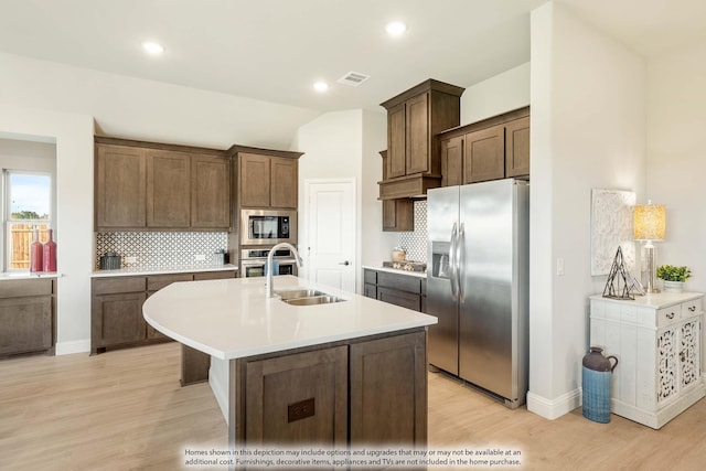 kitchen with stainless steel appliances, tasteful backsplash, sink, a kitchen island with sink, and light wood-type flooring