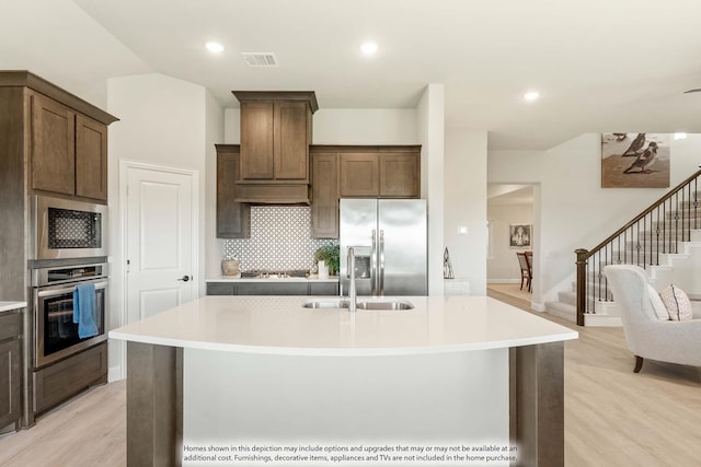 kitchen with light hardwood / wood-style floors, tasteful backsplash, sink, stainless steel appliances, and a center island with sink