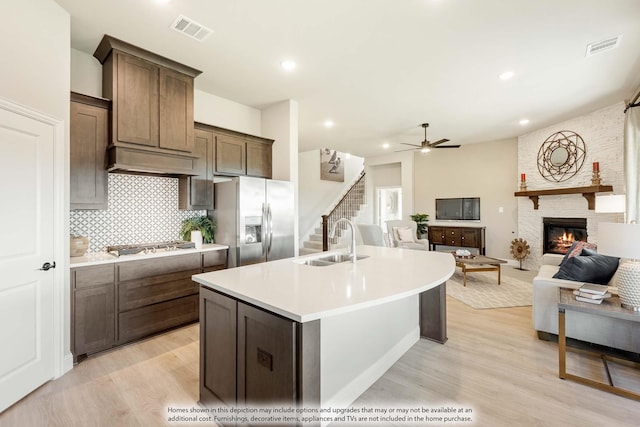 kitchen with a stone fireplace, light hardwood / wood-style floors, appliances with stainless steel finishes, sink, and an island with sink