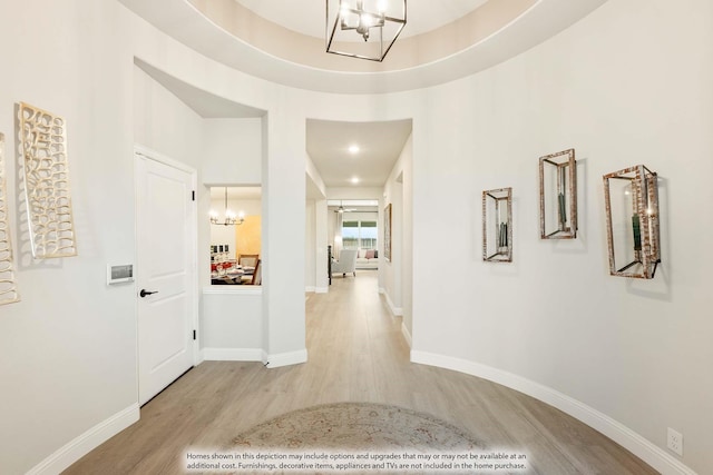 hall featuring light hardwood / wood-style flooring, a raised ceiling, and an inviting chandelier