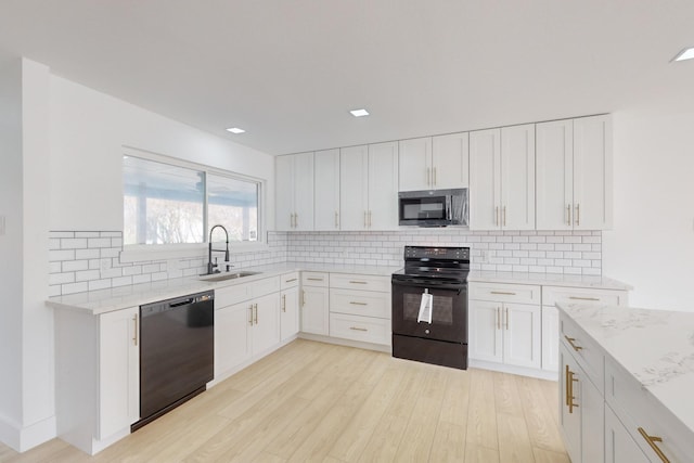 kitchen with black appliances, white cabinetry, sink, light stone counters, and light hardwood / wood-style flooring