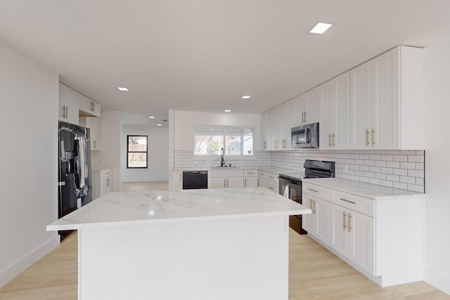 kitchen featuring white cabinetry, tasteful backsplash, light stone countertops, a kitchen island, and black appliances