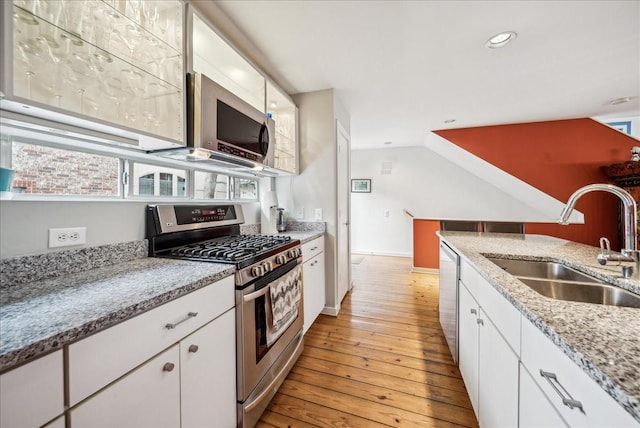 kitchen featuring light stone countertops, white cabinets, stainless steel appliances, sink, and light hardwood / wood-style flooring