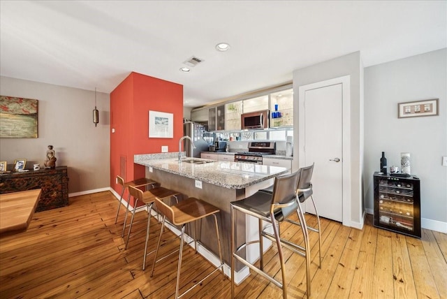 kitchen with light hardwood / wood-style floors, sink, stainless steel appliances, light stone counters, and a breakfast bar area