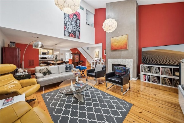 living room with hardwood / wood-style flooring, a tile fireplace, and a towering ceiling