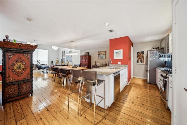 kitchen featuring a kitchen bar, light hardwood / wood-style floors, white cabinets, sink, and stainless steel appliances