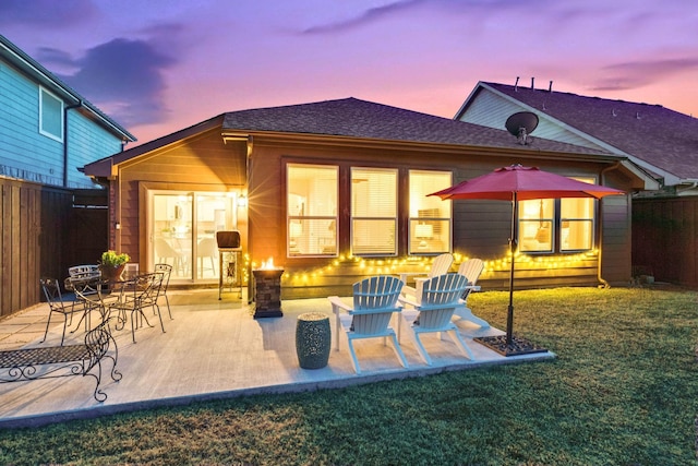 back house at dusk with a patio area and a lawn